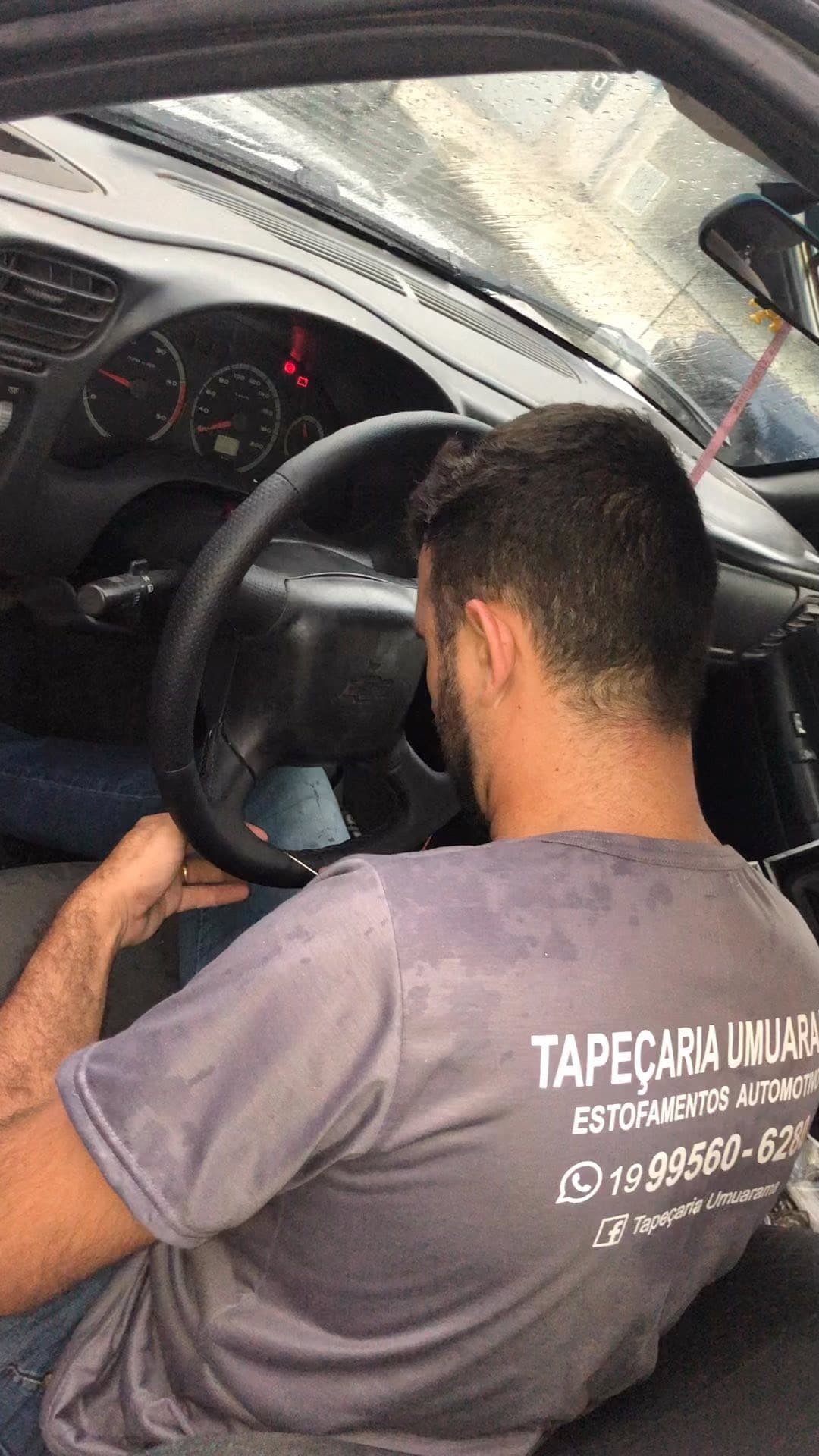 Tapeceiro com camiseta da Tapeçaria Umuarama costurando o revestimento de um volante